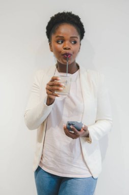 Afro-Amerikalı bir kadın cep telefonuyla kafede dinlenirken samanla buzlu kahve içiyor. Gençlik ve teknoloji.