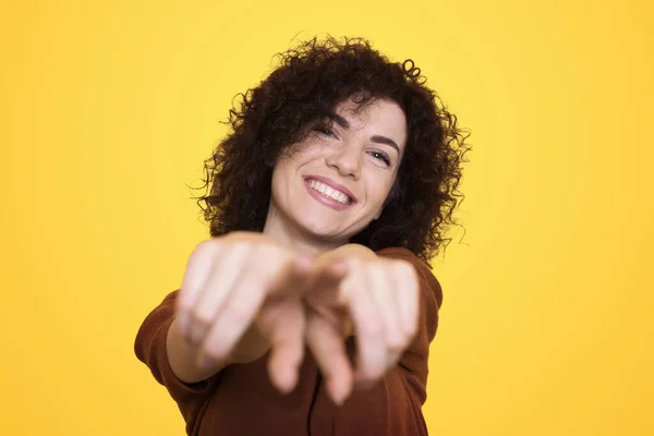 Young brunette woman pointing to you and the camera with fingers, smiling positive and cheerful female isolated over yellow background.