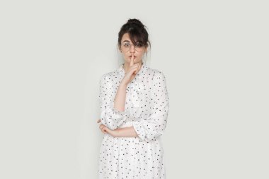 Portrait of young attractive brunette woman wearing dress showing shh gesture isolated on white background. Keep secret