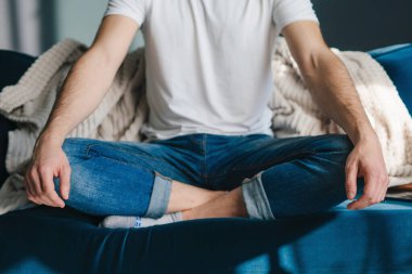 Relaxed man sitting with his legs crossed on the sofa doing some meditation. Cozy apartment. People lifestyle.
