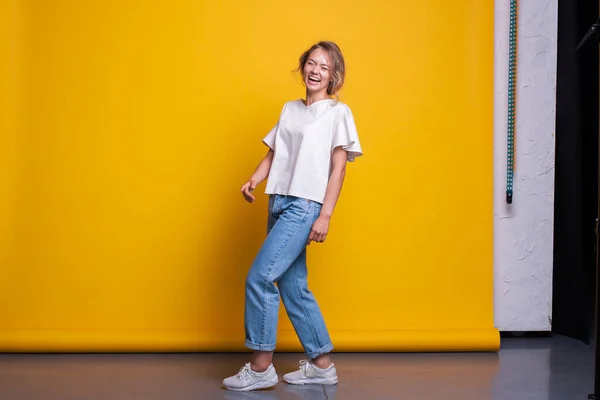 Full length view of amazing good-looking woman wearing jeans standing indoors in studio. Pretty woman laughing. Studio fashion portrait. Full-length studio