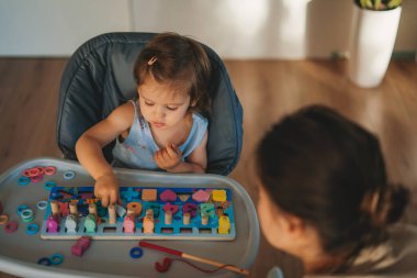 Happy infant sitting on high-chair and playing with wooden toys in modern bright home. Cute baby playing with toys.