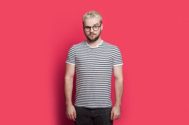 Portrait of skeptical young bearded man looking at camera isolated over pink background.