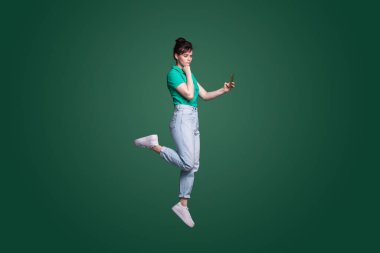 Full length portrait of a thoughtful doubtful woman talking on mobile phone isolated over green background.