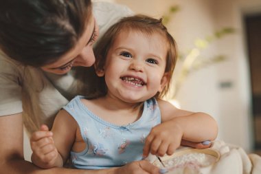 Smiling mom teaching her baby girl embroidering with needles, relaxing together at home. Engaged in hobby activity on weekend