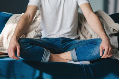 Man meditating, practicing yoga sitting on sofa in lotus pose for exercise, peace and zen fitness. Calm mindset, wellness and healthy balance, praying and relax