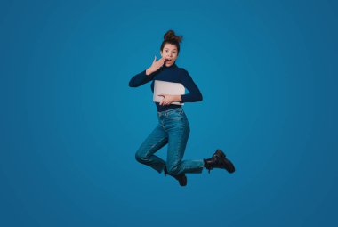 Photo of pretty excited woman jumping holding modern device isolated on blue color background. Digital technology.
