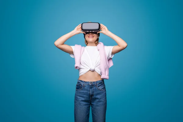 Young woman using augmented reality eyeglasses being in virtual reality isolated over blue background. Futuristic realistic 3d creative concep. Modern