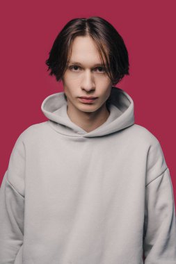 Fashion studio portrait of a young man wearing warm winter trendy fleece hoodie, studio shot, isolated on pink background.