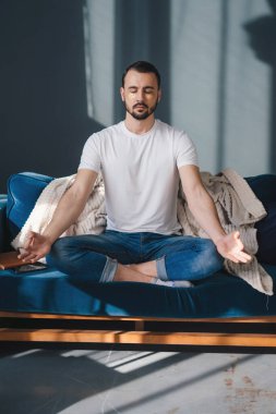 Huzurlu bir milenyum adamı, gözleri kapalı, rahat bir kanepeye uzanıyor ve sabahları evde meditasyon yapıyor. Yaşam dengesi kavramı. Sakin ol, dua et ve rahatla.