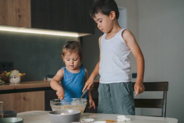 Küçük kız ve erkek doğum günü pastası için malzemeleri bir kasede karıştırıyorlar. Küçük çocuklar mutfakta yemek pişiriyor. Fırın hamuru yoğurur ve kurabiye pişirir..