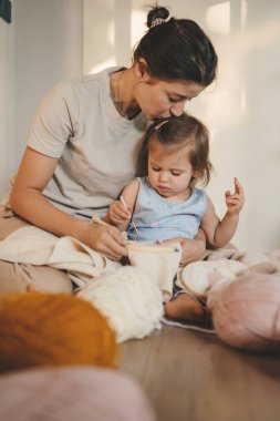 Bir kadın, çocuğuna örgü örmeyi öğretirken elinde nakış iğneleriyle evde vakit geçirir. İnsanların yaşam tarzı portresi. Aile evi eğlencesi. Aile