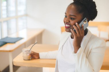 Beyaz ceketli, sevimli, esmer bir kadın bir kafede cep telefonu kullanarak arkadaşıyla telefon görüşmesi yapıyor. İnsanlar, teknoloji ve iletişim
