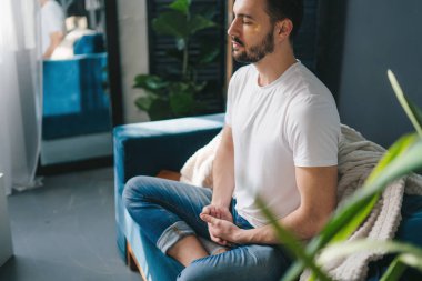 Genç bir adamın yoga yaparken ve oturma odasında rahat bir kanepede meditasyon yaparken fotoğrafı. Sabah rahatlaması ve yoga pratiği konsepti