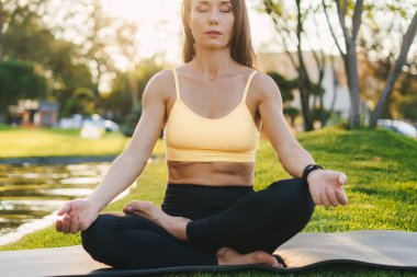 Önde, yoga minderinde oturmuş parktaki gözleri kapalı meditasyon yapan esmer bir kadının portresi. Yoga pozu, iç dengeyi bulmak. Sağlıklı