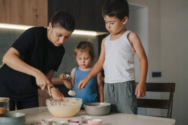 Küçük kız kardeşiyle birlikte tatlı beyaz bir çocuk bovlinge un dökerek, evde kurabiye için hamur hazırlarken malzemeler ekliyor. Yemek kursları. Ekmek ve