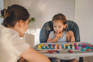 Yüksek sandalyede oturan ve eğitici tahta oyuncaklarla oynayan mutlu beyaz kız. Erken öğrenim kavramı ve iyi motor becerilerin gelişimi