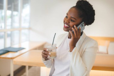 Kahvede buzlu kahve içen, masada oturan ve arkadaşlarıyla telefonda konuşan genç afro kadınlar. İnsanların yaşam tarzı konsepti. Akıllı telefon.