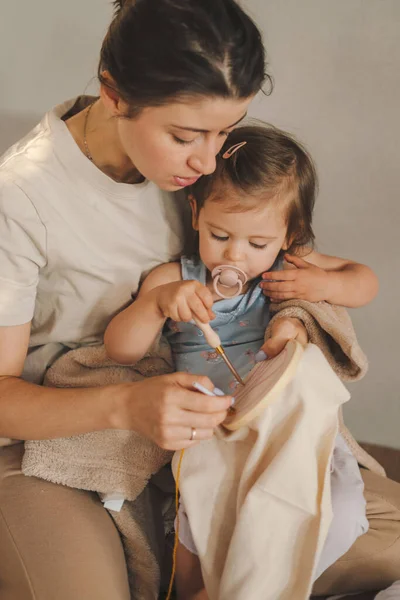 Woman holding her baby child while teaching knit with knitting needles. Mother teaching baby knit, great design for any purposes. Mother holding infant baby.