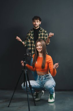 Sosyal medya için kameranın önünde dans eden komik çift videosu, tripodun üzerinde modern cep telefonu, siyah arka plan. Sosyal medyada paylaşılacak video içeriği