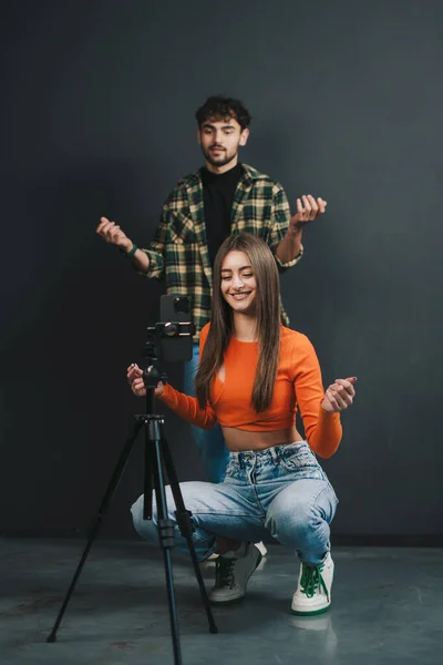 stock image Funny couple recording video for social media dancing in front of camera, modern cell phone on tripod, black background. Video content to share on social media