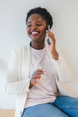 Genç ve çekici Afrikalı kadın boş zamanlarında kafede oturup cep telefonuyla sohbet ediyor. Cep telefonu kullanan bir kadın. İnternet