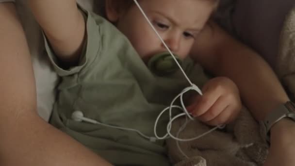 아기는 엄마가 이어폰을 가지고 있습니다 부모와 집에서 있습니다 양육용 침대와 — 비디오
