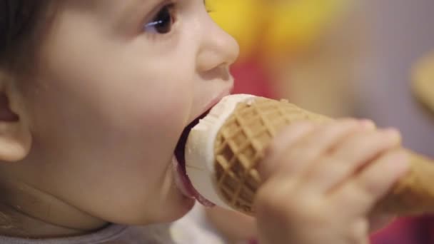 一个有着棕色眼睛的可爱的白人女婴的画像 她在华夫饼蛋筒里吃着并舔着冰淇淋 微笑的情感 关门的肖像 — 图库视频影像