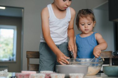 Sevimli küçük kız ve erkek kardeşi mutfakta hamuru karıştırıyorlar. Aile evi eğlencesi. Tatlı yemek..