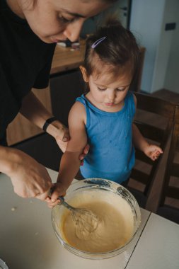 Annesine yardım eden küçük kız pastayı hazırlıyor, çırpıcı kullanarak hamuru karıştırmanın tadını çıkarıyor. Hobi konsepti. Aile evi eğlencesi. Tatlı yemek..