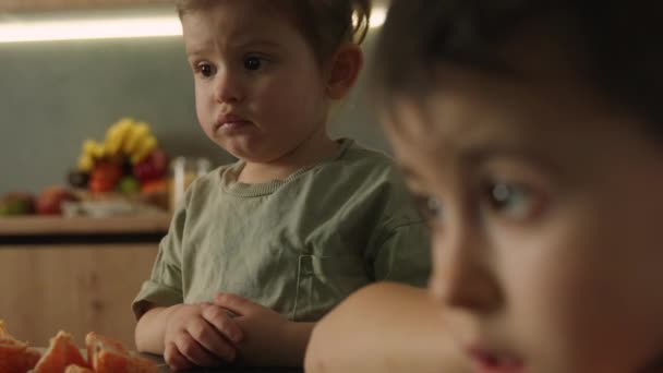 两个孩子沉迷于坐在厨房的桌旁看平板电脑 家庭日的概念 快乐的生活人的生活方式概念 人们的生活方式 — 图库视频影像
