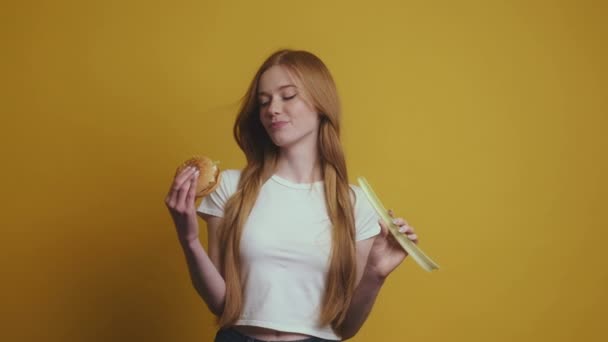 黄色の背景の上に隔離された別の手と野菜でバーガーと2つのオプションの間で選択若い女性 健康食品とファーストフードの概念 — ストック動画