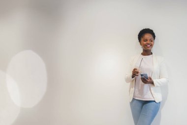 Afro-Amerikalı kadın sosyal medyada geziniyor ve fotokopi alanı olan beyaz bir duvara yaslanarak buzlu kahve içiyor. İnternet bilgileri. Lezzetli