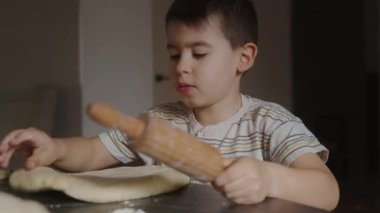 Küçük çocuk, annesine merdaneyle hamuru pişirmesi için yardım ediyor. Ev içinde rahat bir yaşam tarzı, güzel bir çocuk, tatil konsepti, oklava tokası..