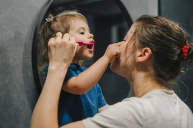 Bebek kızına diş fırçalamayı öğreten bir annenin yan görüntüsü. Banyoda. Mutlu bir aile. Çocuk fırçalamayı, diş temizlemeyi öğreniyor..