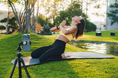 Spor giyim sektöründe yetişkin bir kadın blogcu, kameralı telefondan dışarıda yoga yaparken video kaydediyor. Antrenman egzersizi. Sağlıklı yaşam tarzı, spor