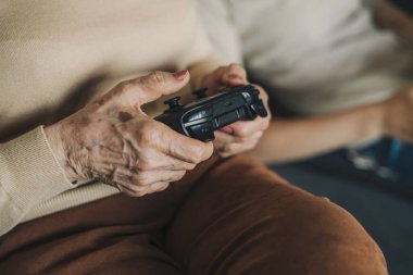 Üst düzey kadın, televizyonda bilgisayar oyunu konsolu kullanarak modern teknoloji cihazıyla oynuyor. Kablosuz kontrolörlü beyaz bir oyuncu evde oturuyor. İnsanlar
