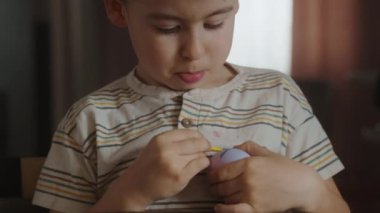 Küçük çocuk paskalya yumurtalarını boyuyor, tatillere hazırlanıyor, mutfakta oturuyor. Paskalya için hazırlık, yaratıcı ev yapımı dekorasyon. Çocuk çocuk eğleniyor ve...