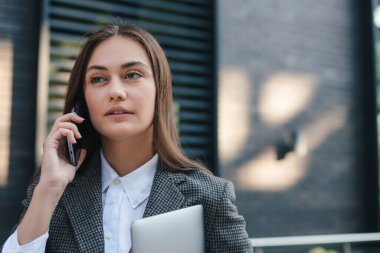 Genç başarılı iş kadını lideri ceketini giymiş dışarıda cep telefonuyla konuşuyor, cep telefonuyla iş görüşmesi yapıyor. Cep telefonu iletişimi