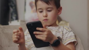 Çocuk kanepede oturmuş akıllı telefon kullanıyor ve rahat bir evde internette oyun oynuyor. Sosyal medya. Tembel hafta sonları faaliyet kavramı.
