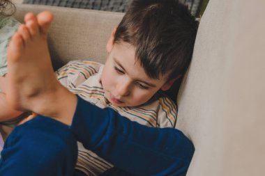 Evcil giysiler giymiş küçük bir çocuk kanepede oturuyor ve evde boş vakitlerini içeride geçiriyor. Salon konsepti