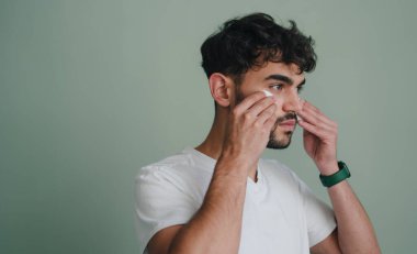Sakallı adamın sabah rutinini pamuk yastıkla yaparken, gri arka planda tek başına dikilirken yan görüntüsü. Cilt bakımı, bakım. Pozitif