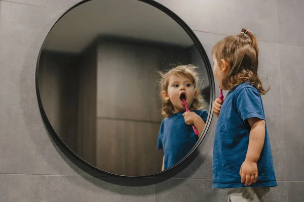 stock image Shot of a little baby girl brushing her teeth in a bathroom in front of a mirror. Morning hygiene. Getting minty fresh breath.