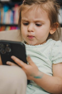 Kız bebek çizgi film izlemek için akıllı telefon kullanmaya çalışıyor. Bebek ve teknoloji konsepti. Fütürist teknoloji. Eğitim, internet teknolojisi. Çalınıyor