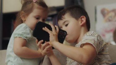 Erkek kardeşi, kız kardeşinin önünde telefonu tutarken ona bir video gösteriyor. Çocuklara internet bağımlılığı. Sanal dünyadaki çocuklar oyunlar oynar.