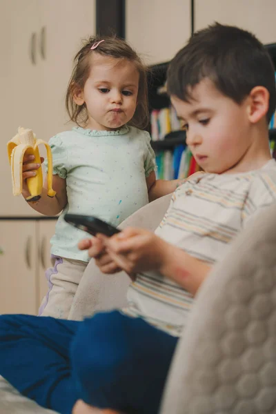 Bebé Comiendo Plátano Mientras Hermano Jugando Juegos Teléfono Concepto Tecnología — Foto de Stock