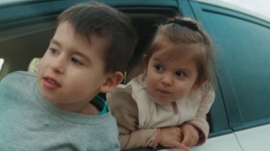 Şaşkın küçük bir çocuk ve kız arabanın camından dışarı bakıyorlar, ön koltukta oturuyorlar ve pencereden dışarı sarkmışlar. Gülümseyen mutlu çocuk. Mutlu