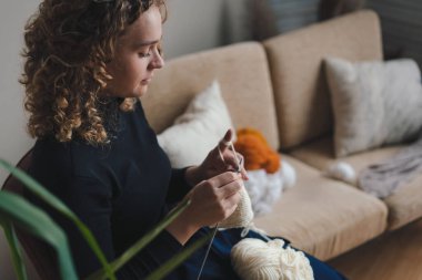 Oturma odasındaki koltukta oturan ve evde hediye olarak eşarp ören güzel bir kadının yan görünüş portresi. Ev hayatı işte. Ev içi rahatlık