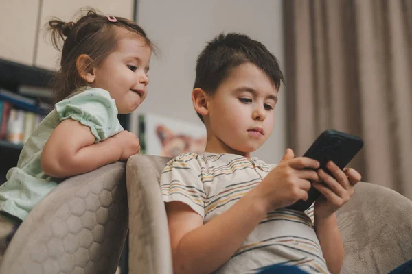 小可爱的兄妹使用智能手机 一起玩 一起看卡通片 沉迷于坐在扶手椅上的科技 教育互联网 — 图库照片