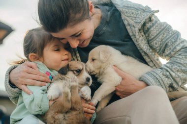 Genç ve güzel bir anne küçük tatlı kızına sarılıyor, dışarıda köpeklerle oynuyor. Arkadaşlık ve bakım kavramı. Arkadaşlık ve aşk